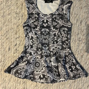 Svartvit peplumtop från Sisters Point - Säljer en snygg peplumtop från Sisters Point i svartvitt mönster. Toppen är ärmlös med rund halsringning och har ett detaljerat blommigt mönster. Perfekt att styla med jeans eller kjol.