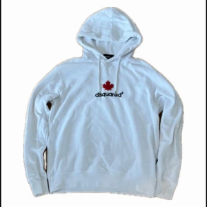 Vit Dsquared2 hoodie med röd lönnlöv - Säljer en vit hoodie från Dsquared2 med en röd lönnlöv och svart logga på bröstet. Tröjan har huva med dragsko och långa ärmar. Perfekt för dig som gillar stilrena och bekväma plagg. Hör av dig vid frågor!