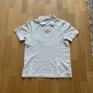 Vit pikétröja från Bläck - Klassisk vit pikétröja från Bläck med krage och korta ärmar. Perfekt för en clean och stilren look. Tröjan är tillverkad i mjuk bomull och har en enkel design utan tryck eller mönster.