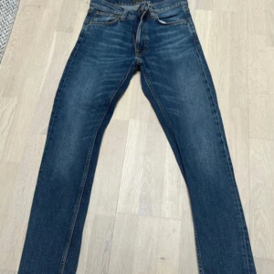 Blå Lean Dean jeans från Nudie Jeans - Säljer ett par klassiska blå Lean Dean jeans från Nudie Jeans. Modellen har en smal passform och är tillverkad i 99% bomull och 1% elastan för extra stretch. Perfekta för dig som gillar en stilren och tidlös look.