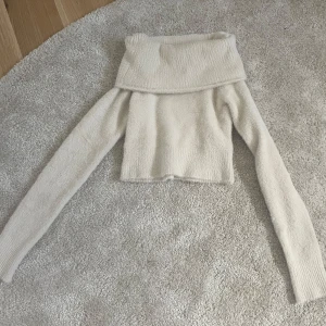 Offshoulder vit stickad tröja från Bershka - Säljer en supermjuk och fluffig offshoulder tröja från Bershka i vitt. Tröjan är stickad, har långa ärmar och en croppad passform. Perfekt för dig som gillar trendiga och bekväma plagg!