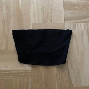 Svart tubtopp från H&M Divided - En enkel svart tubtopp från H&M Divided. Perfekt att styla till olika outfits, tillverkad i mjukt material som sitter bekvämt mot kroppen. Klassisk och stilren design utan axelband.