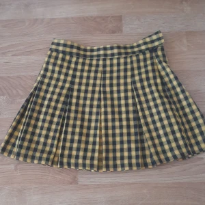 Gul och svart rutig kjol från H&M Divided - Säljer en kort gul och svart rutig kjol från H&M Divided. Kjolen har veckad design och bred linning för en snygg passform. Perfekt för dig som gillar en punkig eller alternativ stil. Ganska så kort, kan va bra att ha i baktanke innan köp.