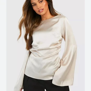 Beige satintopp med vida ärmar - Säljer en elegant beige satintopp med rund halsringning och långa, vida ärmar. Toppen har en mjuk glans och en figurnära passform som ger en lyxig känsla. Perfekt att styla med både byxor och kjol. Färgen är som på första bilden(dåligt ljus). Tyvärr kommer den inte till användning, som ny i skicket, endast använd någon gång💗