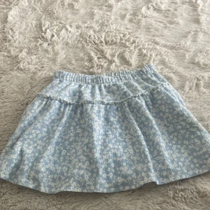 Ljusblå blommig kjol från Zara - Supersöt ljusblå kjol från Zara med vitt blommönster och volangdetalj upptill. Kjolen har resår i midjan och är i ett lätt och luftigt material, perfekt för varmare dagar. PASSAR XS, SUPERBRA SKICK💕💕💕💕PRIS KAN DISKUTERAS