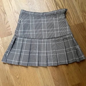 Rutig kortkjol från H&M - Snygg rutig kortkjol från H&M i svart och vit. Kjolen har en dragkedja i sidan och ett klassiskt rutmönster. Perfekt för en stilren look. 