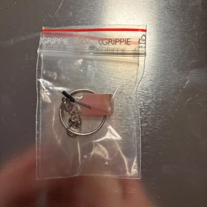 Nyckelring med rosa detalj - Säljer en stilren nyckelring med en rosa rektangulär detalj. Perfekt för att hålla ordning på dina nycklar med en touch av färg. Enkel och praktisk design. 