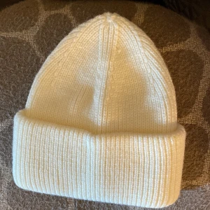 Vit stickad mössa - Snygg vit stickad mössa med ribbad design. Perfekt för kyliga dagar och ger en stilren look. Passar de flesta huvudstorlekar. Oanvänd
