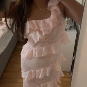 Ljusrosa klänning med volanger - Säljer en ljusrosa klänning från Boohoo med volanger och blommigt mönster. Klänningen har en oneshoulder-design och är perfekt för exempelvis bal. Den har bara testats på och är helt oanvänd samt att prislappen är kvar. Jag säljer för att den tyvärr inte passar mig. Boohoo storlekar är små så även om den är i storlek 40 så passar den storlek 38, det vill säga storlek M. Original pris var 995kr <3