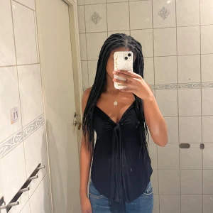 Svart knyt topp - Snygg svart ärmlös topp med knyt framtill. Perfekt för en stilren look och passar bra till jeans eller kjol. Toppen har en v-ringad design som ger en elegant touch.