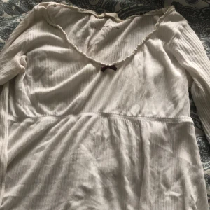 Vit ribbad topp från Odd Molly - Säljer en söt vit ribbad topp från Odd Molly med en liten rosett framtill. Toppen har långa ärmar och en dekorativ kant vid halsringningen. Perfekt för en avslappnad stil.