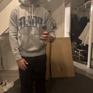 Grå hoodie från Ralph Lauren - Säljer en grå hoodie från Ralph Lauren med stor 'POLO' text i blått på framsidan. Tröjan har en känguruficka och en liten broderad logga på ärmen. Perfekt för en avslappnad stil.