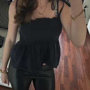 Mörk blå ärmlös topp med knytband - Säljer en mörkblå ärmlös topp med smockdetaljer och knytband vid axlarna. Toppen har en luftig passform och volangkant nedtill. Perfekt för en stilren och bekväm look.