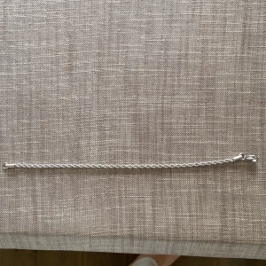 Silverfärgat armband - Snyggt och stilrent silverfärgat armband med en tvinnad design. Perfekt för att ge en elegant touch till din outfit. Armbandet har en enkel låsmekanism som gör det lätt att ta på och av.