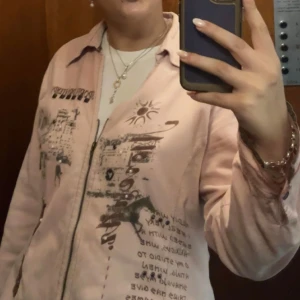 Rosa jacka med bruna tryck  - Säljer denna unika, tunna, rosa jacka med coola tryck och broderade detaljer!! Köpt second hand😇Den är rätt stor med blir snyggt oversize på mig med storlek 38/40💘💘