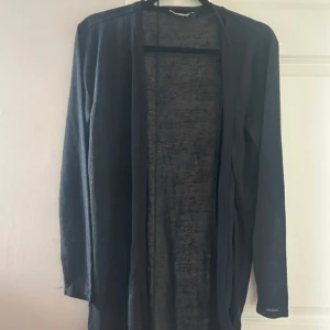 Svart kofta från Angelology - Säljer en elegant svart kofta från Angelology med ett vackert broderi av blommor och en fågel på ryggen. Koftan är långärmad och tillverkad i ett lätt och luftigt material. Perfekt för att lägga till en stilfull touch till din outfit.