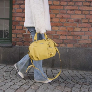 Gul väska  - Snygg gul axelväska med praktisk dragkedja och justerbar axelrem. Perfekt för att lysa upp din outfit med en färgklick. Väskan har även handtag för enkel bärning.