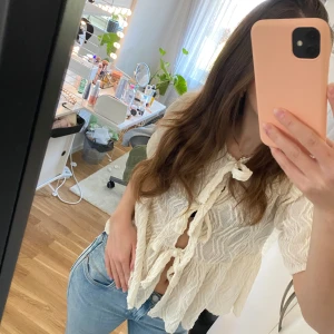 Vit blus med knytning - Säljer en söt vit blus med knytning framtill. Blusen har korta ärmar och ett lätt vågigt mönster i tyget. Perfekt för en avslappnad och stilren look.