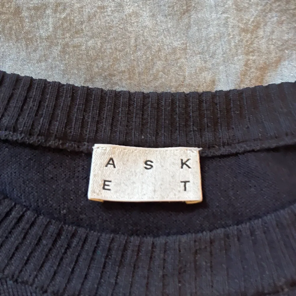 Säljer en stilren svart tröja från Asket i mjuk merinoull. Tröjan har en klassisk rund hals och långa ärmar, perfekt för kyligare dagar. Tillverkad i Rumänien. Passar både till vardags och mer uppklädda tillfällen.. Neuletakit & Villapaidat.