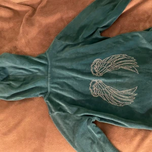 Blå hoodie med vingdetaljer från Pink Republic - Säljer en blå hoodie från Pink Republic med dragkedja och en cool vingdetalj i paljetter på ryggen. Den har långa ärmar och en bekväm passform.