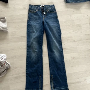 Blå jeans med bootcut - Snygga blå jeans med bootcut och klassisk femficksdesign. De har en knapp och dragkedja framtill samt bälteshällor. Perfekta för en avslappnad stil.