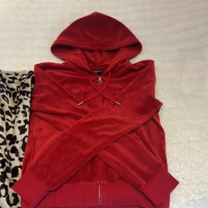 Röd hoodie från Juicy Couture - Säljer en snygg röd hoodie från Juicy Couture. Den har en dragkedja framtill och huva med snörning. Perfekt för en avslappnad stil, allt är kvar på tröjan så super fint skick! 