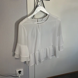 Vit blus från Gina Tricot i storleken S - Säljer en stilren vit blus från Gina Tricot med volangdetaljer. Blusen har trekvartsärmar och en lös passform som ger en luftig känsla.🩷