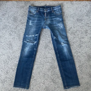 Blå jeans från Dsquared2 - Snygga blå jeans från Dsquared2 med slitna detaljer och en cool look. De har en klassisk femficksdesign och en knappgylf. Perfekta för en avslappnad stil med en touch av edge. Storlek 40: passar folk runt 160-170 cm. Slim fit. Finns o hämta i Halmstad. Den som köper får med en överraskning i paketet, kan vara ett armband eller något liknande