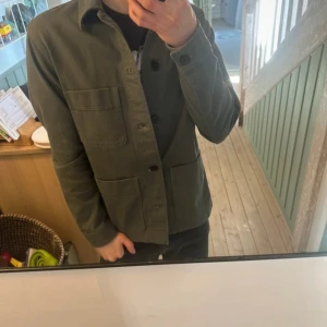 Grön overshirt med knappar - Säljer en stilren grön overshirt med knappar framtill och två stora fickor. Perfekt för lager-på-lager-stil. Passar bra till både vardag och mer avslappnade tillfällen.