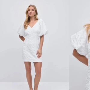 Vit klänning med puffärmar - Säljer en elegant vit klänning med v-ringning och puffiga kortärmar. Klänningen har en strukturerad yta och är perfekt för sommarens festligheter. Den korta längden ger en modern och stilren look.