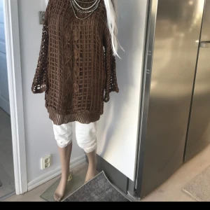 Brun stickad tröja med detaljer - Säljer en brun stickad tröja med ett unikt rutmönster och dekorativa detaljer framtill. Tröjan har långa ärmar och ribbade kanter vid ärmslut och nederkant. Perfekt för en mysig dag hemma eller en promenad i parken. Vet ej storlek men gissar på L