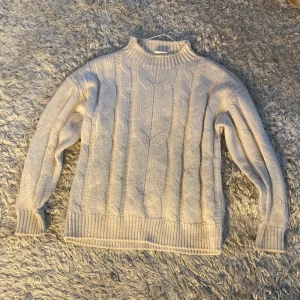 Beige stickad tröja från VILA - Säljer en mysig beige stickad tröja från VILA med ett klassiskt flätmönster. Tröjan har långa ärmar och en ribbad kant vid hals, ärmslut och nederkant. Perfekt för kyliga dagar!
