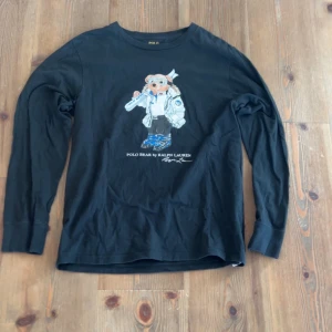 Svart långärmad tröja från Ralph Lauren - Säljer en svart långärmad tröja från Ralph Lauren med ett coolt Polo Bear-tryck på framsidan. Perfekt för dig som gillar en stilren look med en twist. Tröjan är gjord i mjukt material och har en normal passform. Passar perfekt till både jeans och chinos.