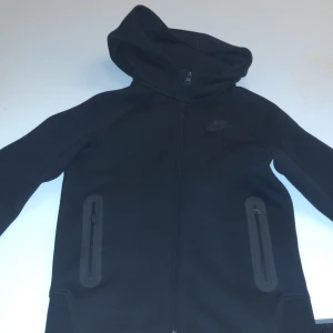 Nike tech - Säljer en stilren svart hoodie från Nike med dragkedja och huva. Denna Nike tech är storlek S men passar M väldigt skön tröja absolut inga defekter elr något sånt skick 9,5/10 använd två gånger. Bara skriva om ni har frågor😃obs det är barn storlek