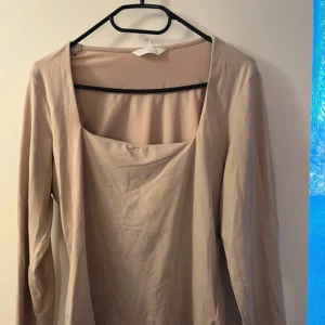 Beige långärmad topp - Säljer en stilren beige långärmad topp med fyrkantig urringning. Perfekt för en minimalistisk look. Passar bra till både jeans och kjol.