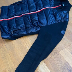 Svart dunväst från Moncler - Snygg svart dunväst från Moncler med dragkedja och ribbade detaljer. Perfekt för kyligare dagar med sin quiltade design och stilrena look. Lappen gick av när ja tvättade det är därför ja säljer den så billigt 