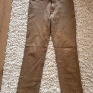 Beige byxor från Sinclair by Kappahl - Snygga beige byxor från Sinclair by Kappahl i storlek 36. Byxorna har en klassisk design med två knappar i midjan och är tillverkade i en stretchig bomullsblandning för extra komfort.  Perfekta för en stilren look.