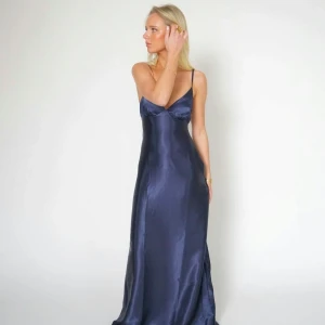 Marinblå balklänning  - Från märket By Stina. Elegant marinblå långklänning i satin med smala axelband och v-ringning. Perfekt för studentbal eller som fin klänning. 