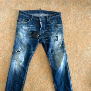 Blå jeans med slitningar från DSQ2 - Snygga blå jeans med coola slitningar och en tvättad look. De har en klassisk femficksdesign och en röd etikett bak. Perfekta för en avslappnad stil med en touch av edge.