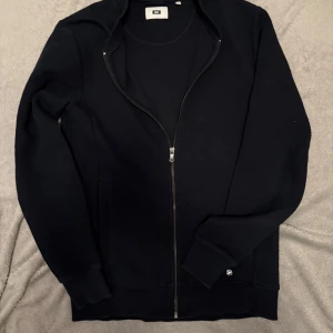 Svart hoodie med dragkedja - Säljer en stilren svart hoodie med dragkedja. Perfekt för en avslappnad look. Den har långa ärmar och en bekväm passform. Perfekt för kyliga dagar. Storlek XS men passar S lika bra