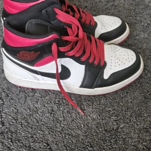 Nike Air Jordans med röd snörning och röd sula - Snygga Nike Air Jordans i svart och vitt med röd snörning och detaljer. Skorna har en klassisk design med perforerad tå och ikonisk logga på sidan. Perfekta för dig som vill ha en stilren och sportig look. Använda en säsong (april-oktober). Lite slitna och något creasade, se bilder, men annars i ett mycket bra skick. 