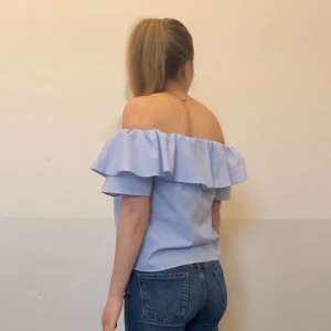 Ljusblå offshoulder topp med volang - Säljer en söt ljusblå offshoulder topp med volangdetaljer. Perfekt för sommardagar och ger en romantisk touch till din outfit. Toppen har korta ärmar och en luftig passform.
