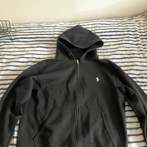 Svart hoodie från Ralph Lauren - Säljer en stilren svart hoodie från Ralph Lauren med dragkedja och klassisk logga på bröstet. Perfekt för en avslappnad look. Hoodien har långa ärmar och en bekväm passform. Pris kan diskuteras 