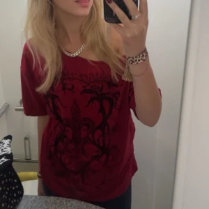 Vinröd topp med tryck - Säljer en vinröd topp med ett svart, detaljerat tryck framtill. Toppen har en lös passform och korta ärmar, perfekt för en avslappnad stil.  💕pris går att diskutera💕
