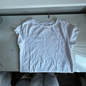 Vit t-shirt från H&M - Säljer en klassisk vit t-shirt från H&M. Den är kortärmad och tillverkad i mjuk bomull, perfekt för en avslappnad stil. Passar bra till jeans eller shorts för en enkel look.