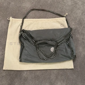 Grå väska från Stella McCartney - Snygg grå axelväska från Stella McCartney storlek M med silver kedjedetaljer. Väskan har en mjuk finish och en rymlig insida med litet fack med dragkedja. Den är använd men fortfarande i väldigt bra skick! Pris kan diskuteras vid snabb affär. 