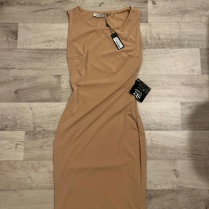 Beige klänning från NLY One - Snygg beige klänning från NLY One i en elegant och stilren design. Klänningen har en tight passform och är ärmlös, perfekt för en chic look. Tillverkad i ett mjukt och bekvämt material.