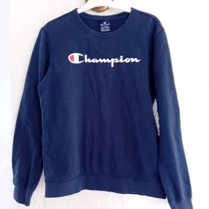Mörkblå sweatshirt från Champion - Säljer en mörkblå sweatshirt från Champion med deras ikoniska logga i vitt och rött på bröstet. Tröjan har långa ärmar och en klassisk rund halsringning. Perfekt för en avslappnad stil.