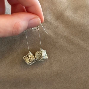 Silvriga örhängen i mycket bra skick - Snygga och unika silvriga örhängen med en kreativ tråddesign. De har en lång krok och en intressant kubformad detalj i tråd. Perfekta för att ge en stilfull touch till din outfit.