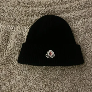 Svart mössa från Moncler - Snygg svart mössa från Moncler med ribbad design och broderad logotyp framtill. Perfekt för att hålla värmen under kyliga dagar.